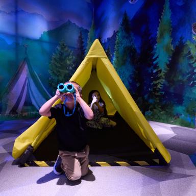 Kids camping and looking through binoculars in the Adventure Zone in Second Story and Beyond